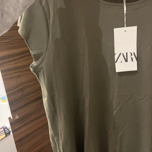 Olivgrön t-shirt från Zara - Säljer en olivgrön t-shirt från Zara i storlek XL. T-shirten har en enkel design med korta ärmar och rund halsringning.  Den är helt oanvänd! Med prislapp kvar. Köptes i somras men inte kommit till användning 