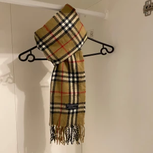 Burberry - Säljer nu denna Snygga halsduk från Burberry i beige. Tillverkad i mjukt lammull med fransar i ändarna.  Den är i mycket fint skick. Perfekt för att hålla dig varm och stilren under kyliga dagar. Hör av er vid funderingar☺️