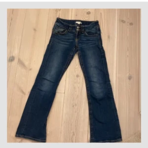 Blå jeans från Gina Tricot - Snygga blå jeans från Gina Tricot med bootcut-stil och lågmidja. De har klassiska fem fickor och dubbla knappar i midjan. 💕 storlek 152!