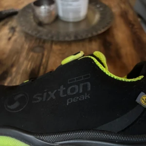 Svarta Sixton Peak skor med BOA-system - Säljer ett par svarta Sixton Peak skor med neongröna detaljer och BOA-snörningssystem. Skorna har en sportig design med förstärkt tå och är perfekta för utomhusaktiviteter.