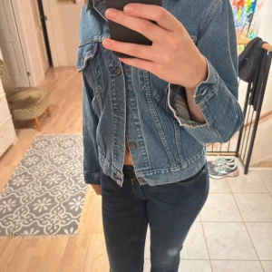 Blå jeansjacka från Levi's - Säljer en klassisk blå jeansjacka från Levi's. Jackan har en normal passform med knappar framtill och två bröstfickor. Perfekt för en avslappnad stil.