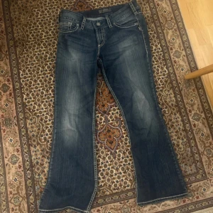 Blå bootcut jeans med broderade bakfickor - Snygga blå bootcut jeans med unika broderade detaljer på bakfickorna. Perfekta för en avslappnad stil med en touch av karaktär. Klassisk femficksdesign och bekväm passform. Lite lösa trådar. Står inte storlek men gissar På m. Midjemått: 40cm+stretch, innerbenslängd: Ca 78cm