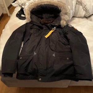 Svart vinterjacka från Parajumpers - Säljer en svart Parajumpers vinterjacka med pälsfodrad huva och flera praktiska fickor. Jackan har en snygg patch på ärmen och gula detaljer. Perfekt för kalla dagar. Nypriset är 12000kr och kvitto finns, jag hjälper min farsa sälja den och den är använd max 3 ggr för han tycker den ser för gangster ut.
