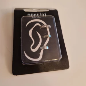 Silverfärgade ear cuffs från Montini - Snygga silverfärgade ear cuffs från Monrini. Ett av örhängena har en rad med glittrande stenar som ger en elegant touch. Perfekt för att ge din look lite extra bling utan att behöva pierca öronen.