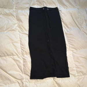 Svart kjol från Boohoo - Säljer en svart längre kjol (3/4) från Boohoo. Kjolen har en slits baktill och ett knytband i midjan för justerbar passform. 