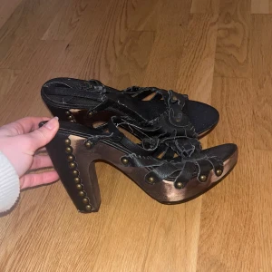 Svarta klackskor med nitar - Snygga svarta klackskor med dekorativa nitar och remmar. Skorna har en robust klack och en unik design. Skorna är små i storleken och passar för personer med storlek 38-39