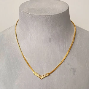 Guldhalsband med V-formad detalj - Elegant guldhalsband med en V-formad detalj prydd med gnistrande stenar. Kedjan är tunn och smidig, vilket ger en stilren look. Perfekt för att lägga till en touch av glamour till din outfit.