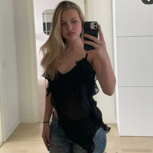 Svart volangtopp från Zara - Snygg svart  topp från Zara med volangdetaljer. Perfekt för en stilren look. Tillverkad i ett lätt och luftigt material.