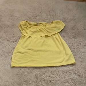Gul offshoulder topp från Lindex - Säljer en söt gul offshoulder topp från Lindex i storlek 146/152. Toppen har en luftig passform och är perfekt för varma sommardagar. Den är tillverkad i ett mjukt och bekvämt material.