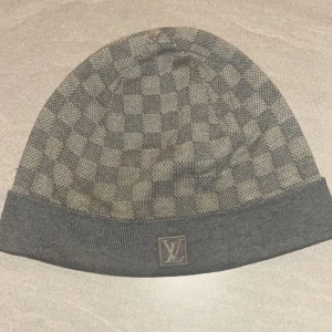 Grå  mössa från Louis Vuitton - LV mössa i nästan helt ny skick. Den har används ett fåtal gånger och är äkta. Säljs på grund av att den inte används längre. Den är ÄKTA. Kan kollas igenom innan man köper. Perfekt till vintern. Priset kan diskuteras. 