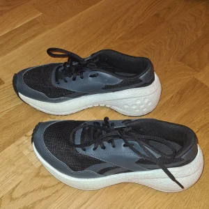 Svarta och grå sneakers från Reebok - Säljer ett par fräscha Reebok sneakers i svart och grått med vit sula. Skorna har använts 2 gånger inomhus och är som nya. Är väldigt lätta att ha på sig och att gå i.