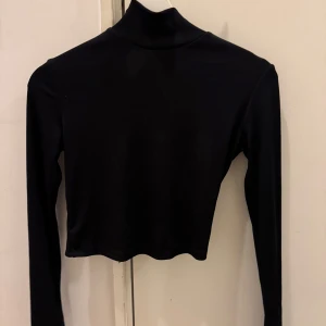 Svart långärmad polotopp - Snygg svart polotopp med lång ärm och en öppen ryggdetalj. Toppen är croppad och har en tight passform, perfekt för en stilren look.