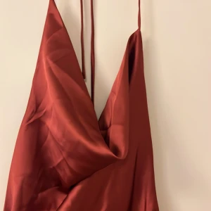 Vinröd långklänning i satin - Elegant vinröd långklänning i satin med smala axelband och v-ringad design. Perfekt för en stilfull kväll.