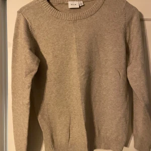 Beige stickad tröja från Vila - Säljer en stilren beige stickad tröja från Vila. Tröjan har en rund halsringning och långa ärmar med ribbade muddar vid ärmslut och nederkant. Perfekt för kyligare dagar!