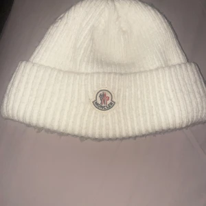 Vit ribbad mössa från Moncler - Snygg vit ribbad mössa från Moncler med broderad logotyp framtill. Perfekt för kyliga dagar och ger en stilren look.