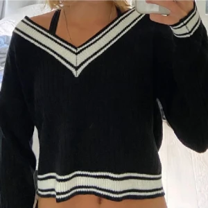 Svart/vit stickad tröja - Snygg svart stickad tröja från H&M i storlek xs med vita detaljer vid halsringning och nederkant. Tröjan har en v-ringad design och långa ärmar, perfekt för en stilren look.