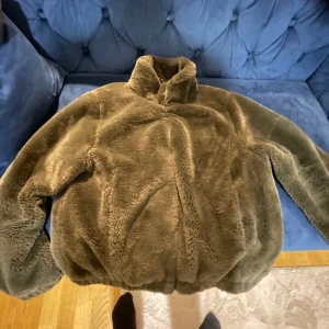 Svart teddyjacka med dragkedja - Mysig brun teddyjacka med dragkedja och hög krage. Perfekt för kyliga dagar med sitt mjuka och fluffiga material. Jackan har en slät insida och långa ärmar för extra värme.