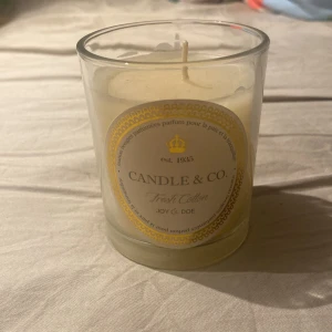 Doftljus Fresh Cotton från Candle & Co. - Elegant doftljus i glasbehållare från Candle & Co. med doften Fresh Cotton. Ljuset har en stilren design med en vit etikett och gulddetaljer. Perfekt för att skapa en fräsch och avslappnande atmosfär i hemmet. Jag fick de av min mamma själv så gillar jag inte doft ljus så säljer har aldrig använt de skriv vid mer frågor
