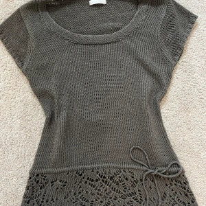 Söt stickad topp med spetsdetaljer - Snygg grå stickad topp med korta ärmar och spetsdetalj längst ner. Toppen har en knytning i midjan som går att justera. DM för frågor💕