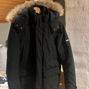 Tommy Hilfiger parkajacka med Päls - Svart parkajacka från Tommy Hilfiger med avtagbar huva och päls. Skick: 9/10. Inköpt för drygt 4000:-  Sitter som mindre M.  Frågor? Tveka inte, hör av dig. 