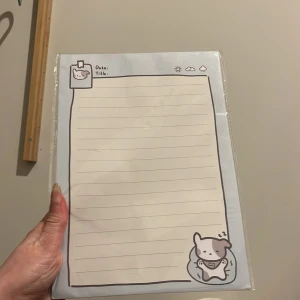 Sött anteckningsblock med hundmotiv - Charmigt anteckningsblock med ett gulligt hundmotiv i hörnet. Blocket har linjerade sidor och en ljusblå kant. Perfekt för att skriva ner datum och titlar. Ett måste för alla som älskar söta skrivbordsartiklar!