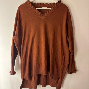 Kilky Tröja  - Snygg tröja i brunt från Kilky med volanger vid halsen och ärmsluten. Tröjan är lite längre baktill. Storleks lapp saknas men upplever den som en storlek L. Smått nopprig se bild 3