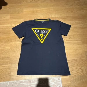 Mörkblå t-shirt från Guess - Snygg mörkblå t-shirt från Guess med det ikoniska gula triangellogotypen på framsidan. Perfekt för en casual look.