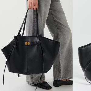 Svart axelväska i skinn - Stilren svart axelväska i skinn med elegant design. Väskan har långa handtag och en praktisk dragkedja för säker förvaring. Perfekt för att bära med sig det nödvändigaste med stil. Aldrig använt, helt ny