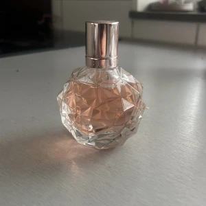 Ari by ariana grande 50 ml  - Elegant parfym i en unik kristallformad flaska med en ljusrosa nyans. Flaskan har en silverfärgad kork och rymmer 50 ml. Knappt använd och inköpt på kicks för ca 2 månader sen. Vita bollen har försvunnit