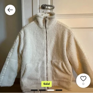 Vit teddyjacka med dragkedja - Mysig vit teddyjacka med dragkedja och hög krage. Jackan har en avslappnad passform och två stora fickor framtill. Perfekt för kyliga dagar.