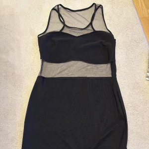 Kort Svart klänning med meshdetaljer - Snygg svart kort klänning med transparenta meshdetaljer upptill och vid midjan. Klänningen är ärmlös och har en tight passform som framhäver figuren