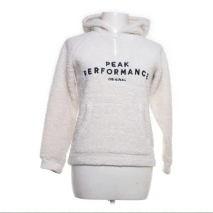 Vit fleece hoodie från Peak Performance - Mysig vit fleece hoodie från Peak Performance med tryck på framsidan. Perfekt för kyliga dagar med sin mjuka och varma design. Har en praktisk huva och långa ärmar. En super varm och skön tröja till vintern.