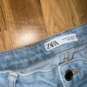 Ljusblå lågmidjade bootcut jeans från Zara - Säljer ett par ljusblå bootcut jeans från Zara. De har en klassisk femficksdesign och knappgylf. Perfekta för en avslappnad stil. (Skrynkliga på bilden då dom behöver strykas) 