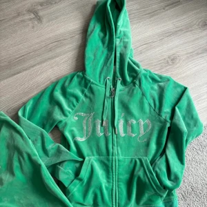 Grön hoodie och byxor från Juicy Couture - Byxorna har storlek xxs och koftan xs. Men sättet passar 34 kanske till och med 36. Säljer en grön hoodie och matchande byxor från Juicy Couture. Hoodien har en dragkedja och texten 'Juicy' i glittriga stenar på bröstet. Byxorna har samma text på baksidan. Perfekt för en avslappnad stil. 