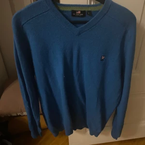 Blå tröja från U.S. Polo Assn. - Säljer en snygg blå tröja från U.S. Polo Assn. med v-ringning och ett broderat emblem på bröstet. Perfekt för en stilren look.