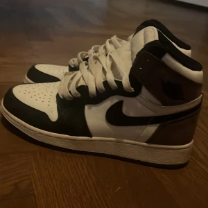 Nike Air Jordans 1 Mocha - Snygga Nike Air Jordans i svart och vit med klassisk snörning. Skorna har en hög design med perforerade detaljer på tån för extra ventilation. Perfekta för en stilren look.