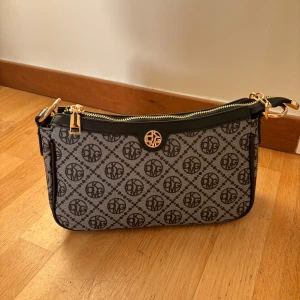 Mönstrad axelväska med gulddetaljer - Snygg axelväska med ett elegant mönster och gulddetaljer. Väskan har en dragkedja och en justerbar axelrem med kedja. Perfekt för att ge din outfit en stilfull touch.