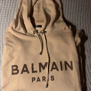 Beige hoodie från Balmain - Riktig fet  beige hoodie från Balmain med stor logga på framsidan. Nypris 10 000kr, kvitto finns.  Storlek L. Passa på att göra ett sjukt kap. Denna färgkombo och modell är slutsåld sedan länge och eftertraktad. Använd sporadiskt några gånger men lite för stor för mig. Aldrig tvättad! 
