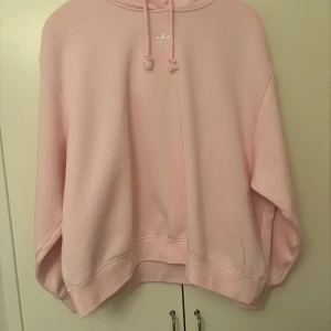 Rosa hoodie från Adidas - Säljer en mysig rosa hoodie från Adidas. Den har en klassisk design med dragsko i huvan och ribbade muddar. Perfekt för en avslappnad stil.
