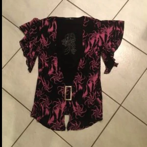 Svart och rosa mönstrad topp - Snygg svart klänning med rosa mönster och korta ärmar. Den har en dekorativ bältesspänne framtill och ett unikt mönster som ger en cool look.