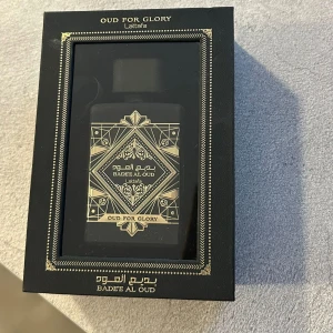 Lattafa Oud For Glory Badee Al Oud Eau de Parfum - Elegant parfym från Lattafa, Oud For Glory Badee Al Oud, i en stilren svart flaska med guldmönster. Doften är rik och lyxig, perfekt för den som älskar orientaliska noter. Flaskan rymmer 100 ml och kommer i en exklusiv förpackning. Helt ny