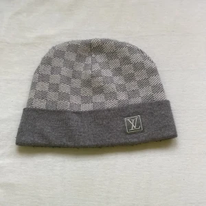 Grå rutig mössa  - Snygg grå mössa med rutigt mönster . Den har en uppvikt kant med en diskret logotyp. Perfekt för att hålla sig varm med stil. och bra skick ingen flickor nåt priset diskuterar snabb affär.