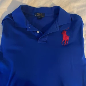 Blå pikétröja från Ralph Lauren - Snygg blå pikétröja från Ralph Lauren med röd broderad logga på bröstet och en stor röd siffra 3 på armen .är en storlek L i kids men passar s oc xs