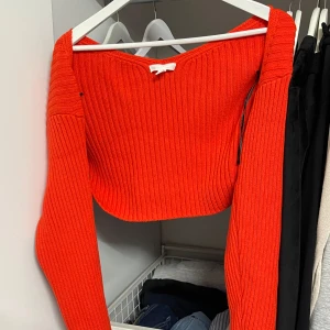 Orange stickad bolerotopp från H&M - Säljer en superfin orange stickad bolerotopp från H&M. Perfekt för höst och vår med sin ribbade design och långa ärmar. Toppen är croppad och ger en snygg look över en enkel t-shirt eller klänning. Perfekt för att lägga till lite färg i garderoben!