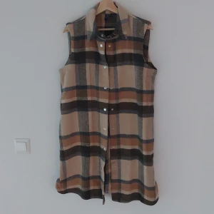 Rutig väst från Vero Moda - Säljer en superfin rutig väst från Vero Moda i storlek M. Västen har ett klassiskt rutmönster i beige, brun och svart. Den är ärmlös och har knappar framtill. Perfekt för höst och vår, och kan stylas både till vardags och fest!