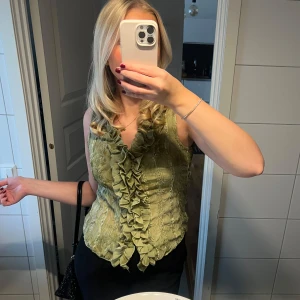 Grön ärmlös topp med volangdetaljer - Säljer en snygg grön ärmlös topp med volangdetaljer framtill. Toppen har en tight passform och är superbekväm att bära💚