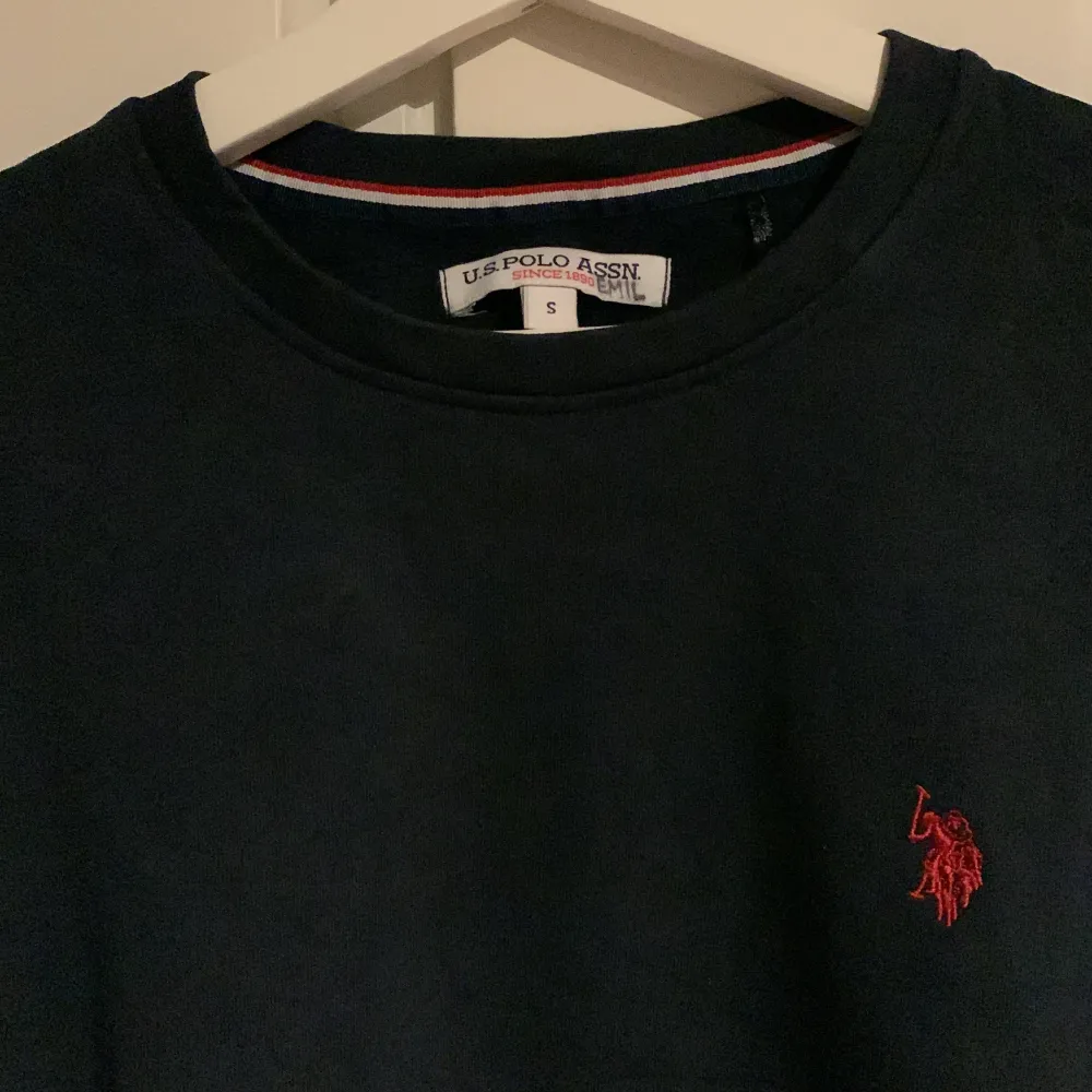 Säljer en snygg och stilren mörkblå tröja från U.S. Polo Assn. Tröjan har en liten röd logga broderad på bröstet och är perfekt för både vardag och lite finare tillfällen. Den är långärmad och gjord i ett mjukt material som känns skönt mot huden.. Tröjor & Koftor.