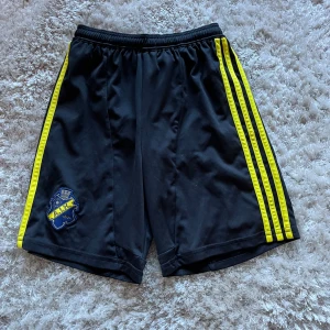 Svarta sportshorts från Adidas med gula detaljer - Säljer nu ett par riktigt sköna AIK shorts 🔥🔥De är knappt använda så de e i ett riktigt bra skick🔥Priste gå att förhandla och skriv om fler frågor eller bilder🤩🤩🤩