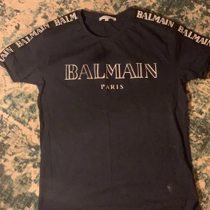 Mörkblå t-shirt från Balmain - Snygg mörkblå t-shirt från Balmain med logotypen tryckt på bröstet och längs ärmarna. Perfekt för en stilren look med en touch av lyx. Passar bra till både jeans och kjol. 