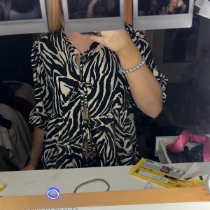 Zebramönstrad blus med knyt - Trendig zebramönstrad blus med knyt framtill. Blusen har trekvartsärmar och en lös passform, perfekt för en stilren look. 🦓✨